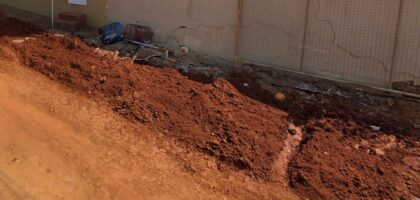 Terra de obra municipal acumulada junto a muro de residência com rachaduras, exemplo de dano causado por obra da prefeitura