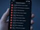 Mão segurando celular com tela cheia de comentários agressivos, em luz azul fria