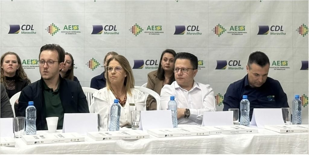 Mesa da plenária regional da Facisc em Maravilha, com banner da CDL e da AESC ao fundo